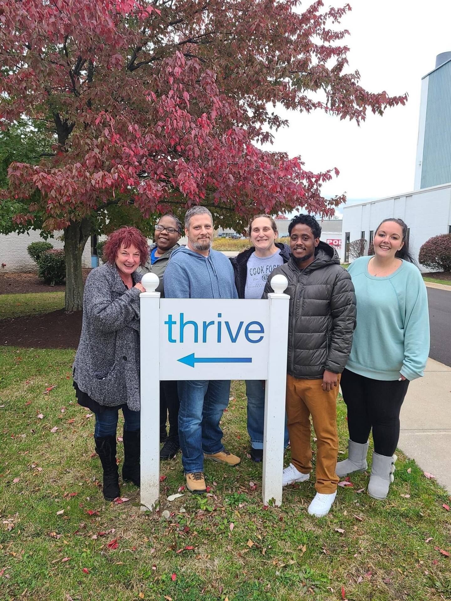 A group of Thrive Peer Recovery Services employees standing outside by the organization's sign.